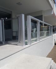 Balcón con barandilla de cristal y metal junto a la playa, edificio moderno al fondo.