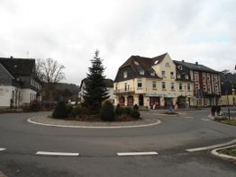 Kreisverkehr mit geschmücktem Baum in der Mitte, umgeben von Gebäuden und leicht bewölktem Himmel.