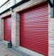 Brick garage with red shutter doors and a small dog looking up at the light.