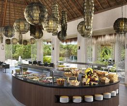 Mesa de buffet en un restaurante con lámparas colgantes y ventanas al exterior.