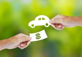 Hands exchanging cutouts of a car and a dollar bill against a green blurred background.