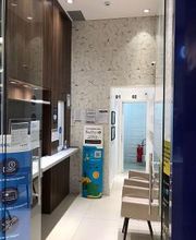 Corredor interior com cadeiras, placas informativas, paredes revestidas e porta de vidro.