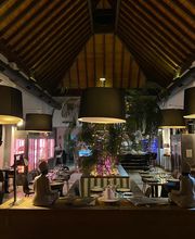 Restaurante elegante con techo alto y lámparas grandes, mesas decoradas y pocas personas presentes.