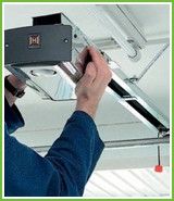 Person adjusting a garage door opener on a ceiling-mounted track.