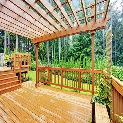 Wooden deck with pergola, overlooking a lush green garden and forest in the background.