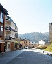 Calle con casas y torre de piedra, montaña al fondo, día soleado.