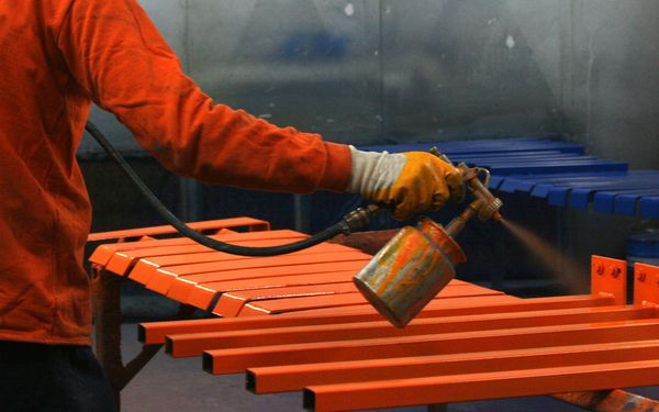 Person lackiert einzelne Stahlbauteile in knalligem Orange.