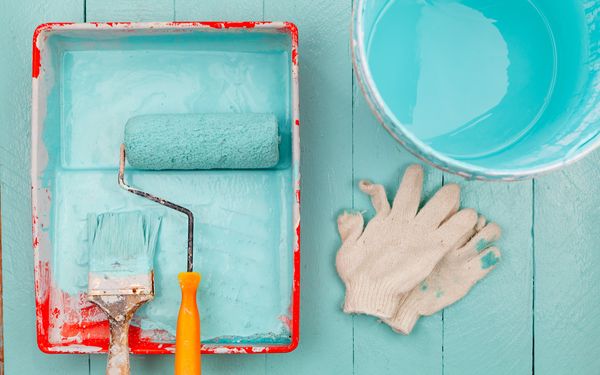 Malerrolle, Pinsel, Handschuhe und Farbeimer mit tandfürkisfarbener Warbe auf einem Holzboden.