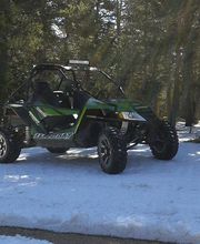 Vehículo todoterreno verde y negro estacionado en un camino nevado rodeado de árboles altos.