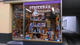 Wollgeschäft mit bunten Garnknäueln und Teddybären im Schaufenster, Beschriftung "Strickbär".