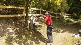 Mann mit rotem Shirt streicht im Wald einen Zaun an.