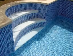 Escalera curva de azulejos azules en piscina, con agua cristalina.