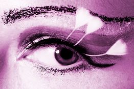 Nahaufnahme eines Auges mit lila Filter, dekoriert mit schwarzem Make-up und weißen Federn.