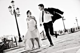 Brautpaar läuft lachend auf Kopfsteinpflaster, er trägt das Sakko über der Schulter.