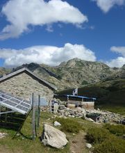 Casa de piedra con paneles solares en las montañas bajo un cielo azul con nubes esponjosas.