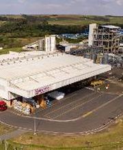 Vista aérea de uma fábrica cercada por áreas verdes em dia ensolarado.