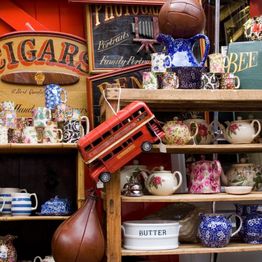 Vintage shop display with floral teapots, a double-decker bus model, and antique signs.