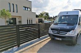 Transporter neben einem modernen Zaun und einem weißen Gebäude im Hintergrund.