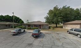 Small parking lot with three cars in front of brick buildings and trees.