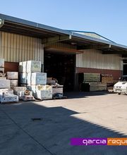 Nave industrial con palés apilados y una furgoneta estacionada frente a la entrada.