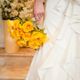 Bride holding a bouquet of yellow roses, standing on stairs in a flowing white wedding dress.