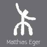 Abstrakte weiße Figur auf grauem Hintergrund, darunter der Text "Matthias Eger".