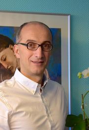Ein Mann mit Brille und weißem Hemd steht vor einem Kunstbild und einer weißen Orchidee.