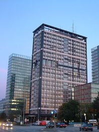 Hohes modernes Gebäude bei Dämmerung, umgeben von Glasbauten und Straßenverkehr.