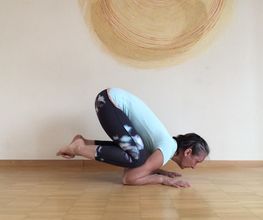 Frau in Yoga-Haltung auf Holzboden vor beiger Wand mit rundem Kunstwerk.