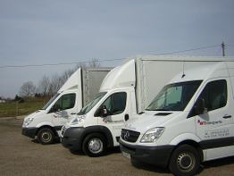 Drei weiße Transporter auf einem Parkplatz, mit einem Logo und Kontaktdaten auf den Seiten.