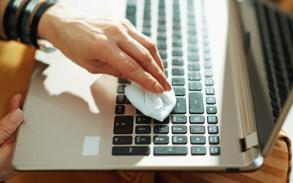 Eine Frau reinigt die Tastatur ihres Laptops mit einem Desinfektionstuch.