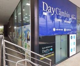 Fachada de uma casa de câmbio com o nome "DayCâmbio" e um cartaz azul.