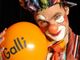 Ein Clown mit weiß geschminktem Gesicht hält einen orangefarbenen Ballon mit "Galli".