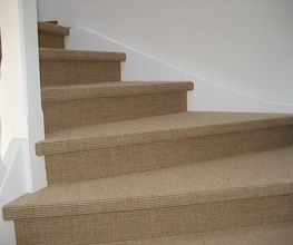 Braune, mit Teppich belegte Treppe mit weißem Geländer, die um die Ecke führt.