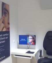 Kamer met een oogmeetstoel, poster over contactlenzen en een computermonitor met een gezicht.