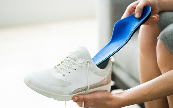 Person legt orthopädische Einlage in einen weißen Sneaker.