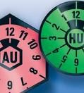 Rosa und grüne Prüfplaketten für Abgasuntersuchung (AU) und Hauptuntersuchung (HU).