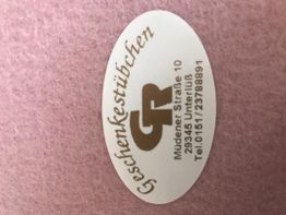 Ein ovaler Aufkleber mit der Aufschrift "Geschenkesstübchen" auf rosa Hintergrund.