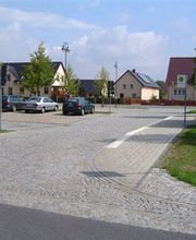 Parkplatz mit Kopfsteinpflaster, ein paar Autos, Häuser im Hintergrund, blaues "P"-Schild.