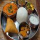 Indian thali with rice, curry, samosa, yogurt, and pickles on a metal plate.