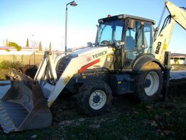 Retroexcavadora Terex blanca estacionada en un terreno con césped y árboles al fondo.