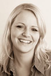 Eine lächelnde Frau mit langen, blonden Haaren in einem gestreiften Hemd im Porträtfoto.