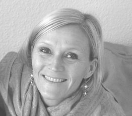 Frau mit lächelndem Gesicht, kurzen blonden Haaren und Ohrringen, in einem Schal gehüllt.