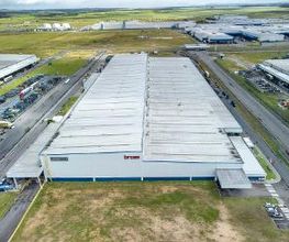 Vista aérea de um grande galpão industrial em um parque logístico com estradas ao redor.