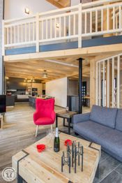 Intérieur moderne en bois avec canapé gris, fauteuil rouge et cuisine ouverte en arrière-plan.