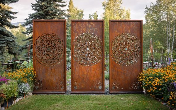 Drei rostbraune Sichtschutz-Elemente mit Mandala-Muster in schönem Garten.