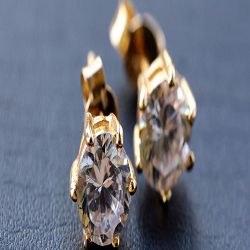 Close-up of gold earrings with sparkling gemstones on a dark surface.