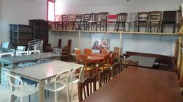 Sala piena di sedie e tavoli di vari stili, alcuni accatastati su scaffali.