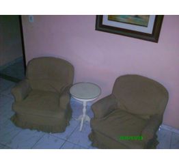 Duas poltronas marrons e uma mesa branca entre elas em uma sala com parede rosa e piso de azulejo.