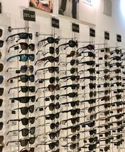 Fila de gafas de sol exhibidas en una pared de una tienda, con descuentos del 20%.